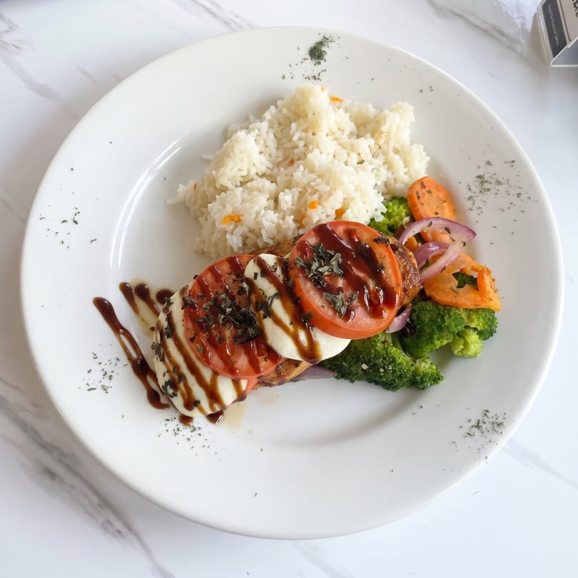 Chicken Caprese with rice, broccoli, carrots, and red onions on a white plate.