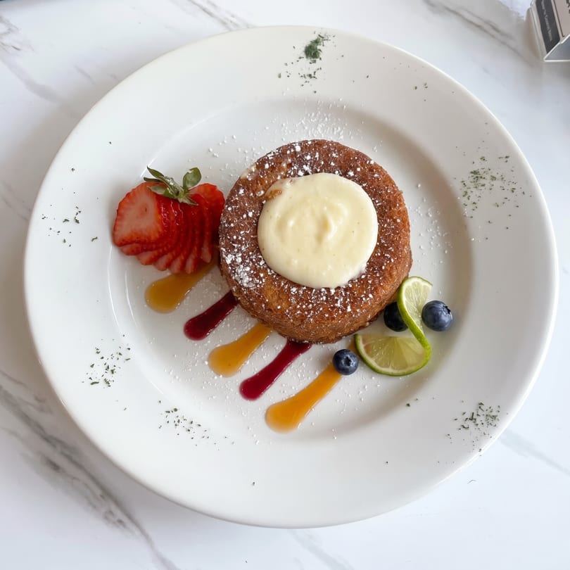 A round dessert with cream, powdered sugar, sliced strawberries, blueberries, lime, and colorful sauces.