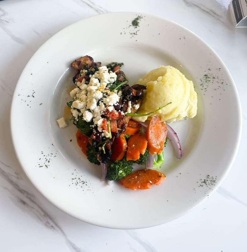A white plate with mashed potatoes, roasted vegetables, and a feta-topped chicken dish.