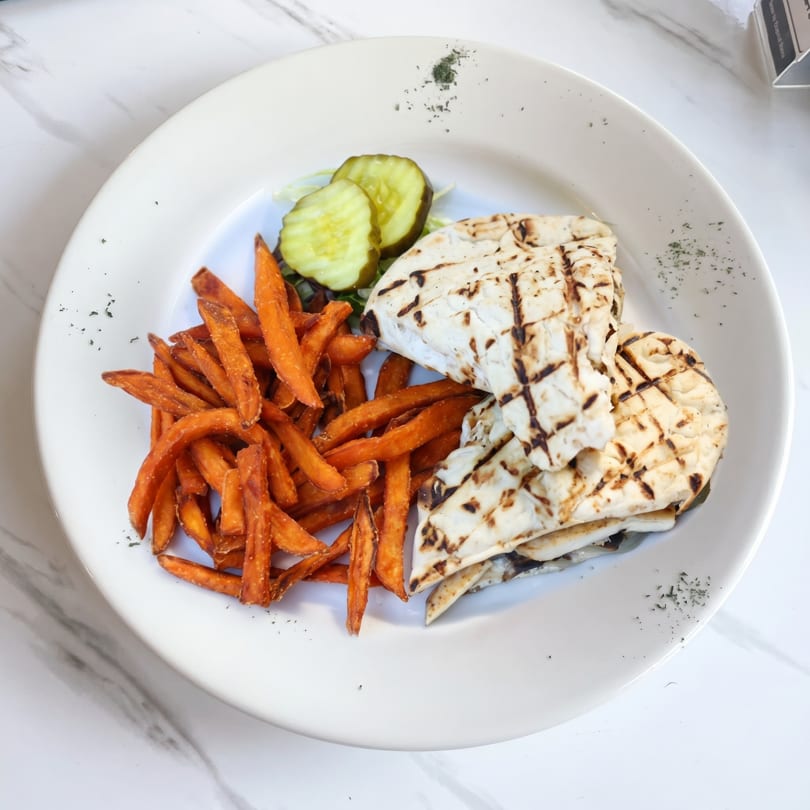 Grilled chicken pita wraps with sweet potato fries and pickle slices on a white plate.
